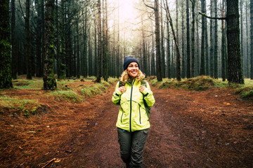 Happy hiker caucasian woman smile and enjoy the nature walking in a forest with high trees - alternative outdoor leisure activity and vacation lifestyle - sun in backlight and mist concept