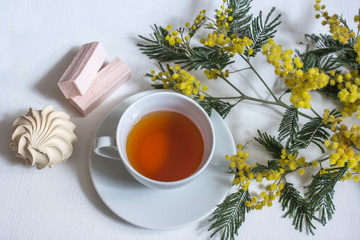 a Cup of black tea, sweets and a Mimosa branch on a white background