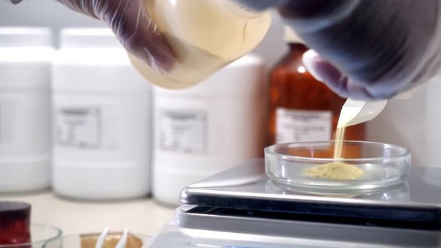 Laboratory worker working with scales. Close-up of chemist wearing gloves from can of puts quicksand on glass cup for weighing in chemical laboratory
