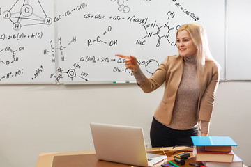 Teacher teaching how to count on whiteboard in classroom. Smiling blonde woman explaining additions...
