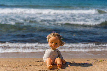 Old Broken Toy Doll Sitting on a Beach in Italy