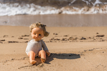 Old Broken Toy Doll Sitting on a Beach in Italy