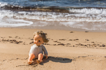 Old Broken Toy Doll Sitting on a Beach in Italy