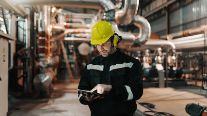 Caucasian worker in heavy industry plant with helmet and in uniform using tablet for work.