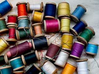 Old multi-colored coils lie in a box. A pile of coils with colored threads. Sewing supplies. Many coils of thread.