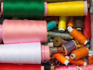 Old multi-colored coils lie in a box. A pile of coils with colored threads. Sewing supplies. Many coils of thread.