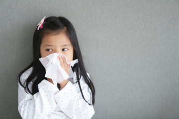 Asian child or kid girl sick and sad with sneezing on nose and cold cough on tissue paper because influenza and weak or virus and bacteria from dust weather and kindergarten school for medical BG