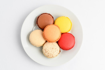 Group of six sweet French macarons on a white plate, isolated on white, flavours of  lemon, caramel, vanilla, coconut and chocolate,  pastel colors