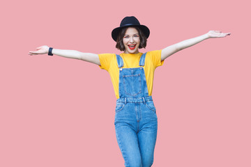Portrait of excited beautiful young woman in yellow t-shirt, blue denim overalls, makeup, black hat...