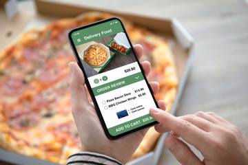 female hands holding phone with delivery food app pizza box - obrazy, fototapety, plakaty