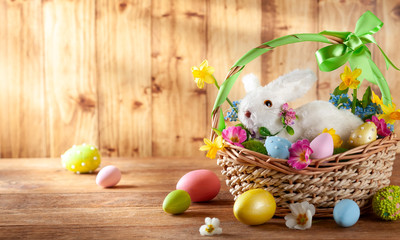 Easter composition with bunny in basket, spring flowers and colorful Easter eggs .