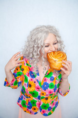 cute chubby girl with white curly hair in a summer jacket with flowers holds a sweet pastry bun in the shape of a heart