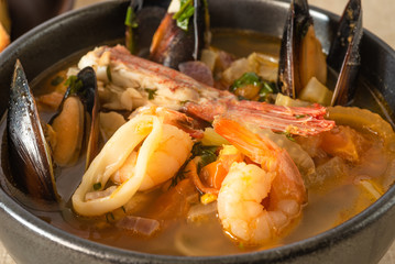 Traditional Mediterranean seafood stew in a black bowl closeup.
