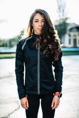 Portrait of young female athlete wearing sport jacket and tights posing outdoors before training...