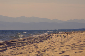 Sandy beach stretching away into the distance and the silhouette of the mountains on the horizon in a light fog. Nobody.