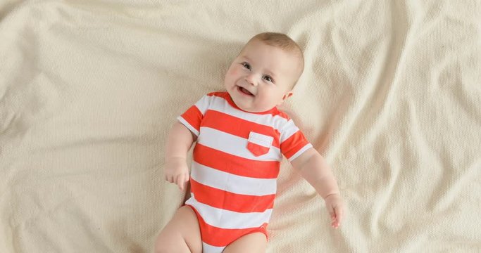 Top view of the baby looking in the camera and smiling, close up 4k shot. A cute little baby is look and smile. Babyboy looks around and smiles and laughs, view drom above
