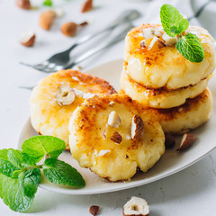 Breakfast Food Delicious Concept. Cottage cheese pancakes, syrniki, curd fritters with honey and huts on white concrete table background. Close-up