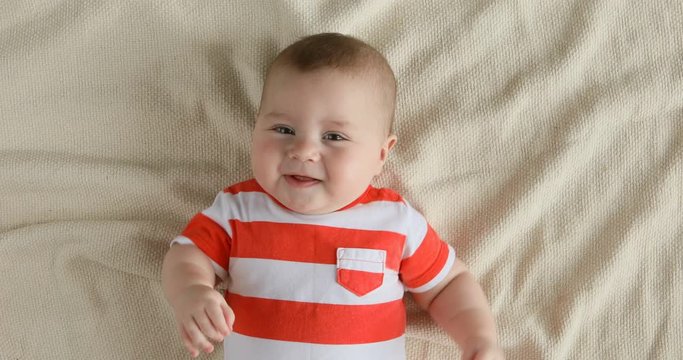 Top view of the baby looking in the camera and smiling, close up 4k shot. A cute little baby is look and smile. Babyboy looks around and smiles and laughs, view drom above