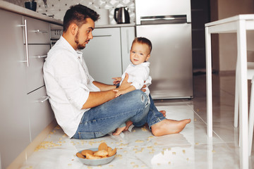 Little boy sitting on a floor. Handsome father in a white shirt.  Family in a kitchen