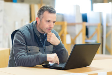 male worker looking at laptop in workshop - Powered by Adobe