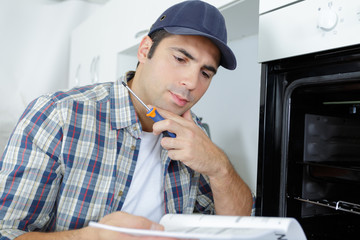 young male electrician fixing oven in kitchen