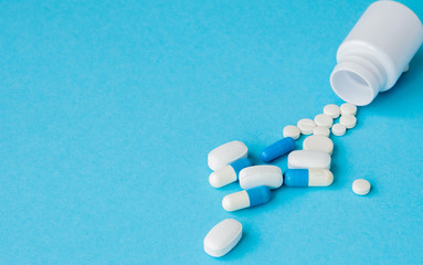 Close up pills spilling out of pill bottle on blue background. Medicine, medical insurance or pharmacy concept - obrazy, fototapety, plakaty