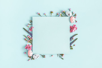 Easter composition. Easter eggs, flowers, paper blank on pastel blue background. Flat lay, top view, copy space - 253943249