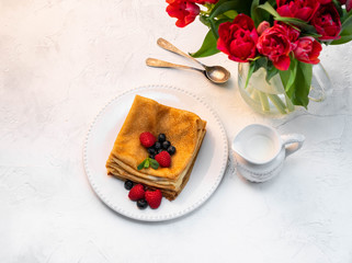 pancakes and berries on white plate on a light backdrop, fresh red tulips