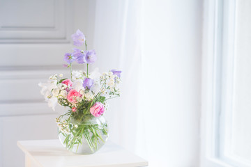 Bedside table, vase with rose and lilac flowers.  White background. Copy space