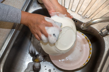 Hand cleaning of female or housewife woman washing dishes with a yellow sponge in kitchen sink