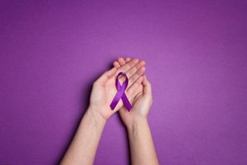 Hands holding Purple ribbons on a purple background. World epilepsy day.