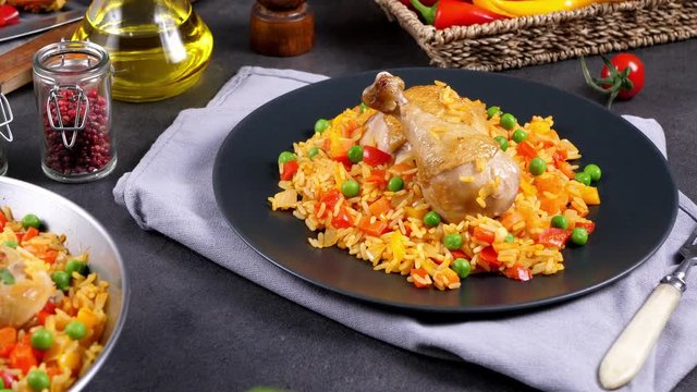 Cooking, steaming, eating, watching. Slow motion. Arroz con pollo. Baked pieces of chicken with bone, rice with paprika and peas. Black background. Served on black plate or spanish pan. 