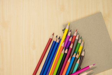 colorful pencils and notebook on wooden background top view. art equipment.