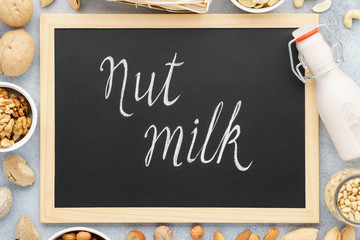 Nut milk and various nuts around chalkboard. Vegan milk.