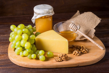 Cheese with grapes, olive, honey on wood