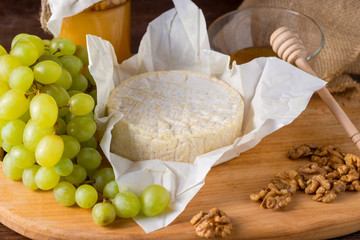 Camembert cheese on a wooden board with honey, fruits and nuts