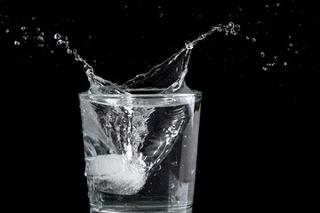 splash from a falling piece of ice into a glass of water on a dark background