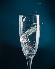 splash in a champagne glass against falling water on a dark blue background