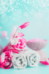 Fototapeta na wymiar Spa towels with pink flowers at light blue background with bokeh. Beauty concept