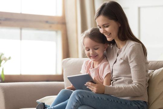 Happy mom and kid daughter using digital tablet on sofa
