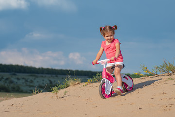 Naklejka premium Good luck kids, laughter and joy. Baby sport. Overcoming difficulties and new routes. Baby girl riding on pink bicycle in the city park for children.