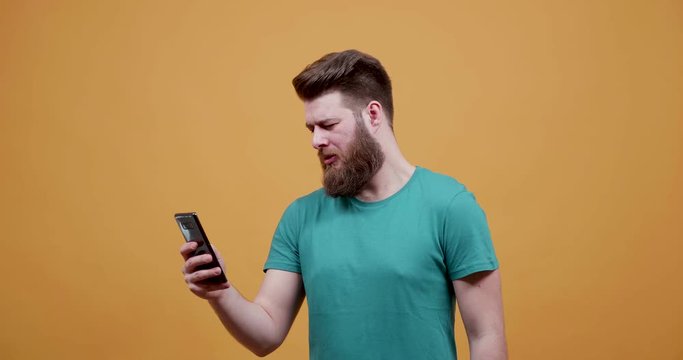 Man looking at funny pictures and videos at his phone in front of an yellow background. Handsome young man with beard looking at his phone screen and laughs.