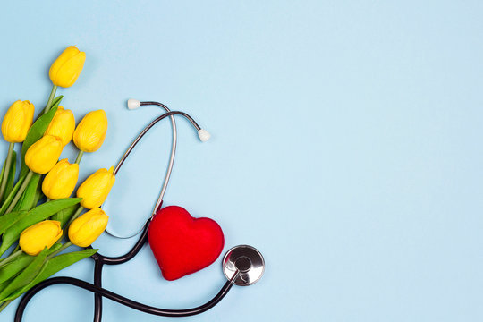 Bunch of yellow tulips with stethoscope and heart on blue background. National Doctor's day. Happy nurse day.