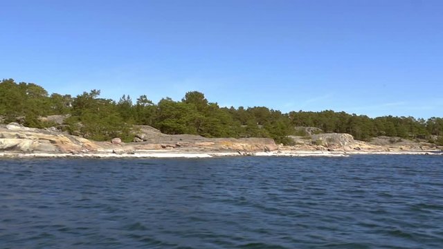 Slow motion tracking shot, from a boat of fresh green islands, in saaristomeri national park, in the finnish archipelago, on a sunny summer day, in Varsinais-suomi, Finland