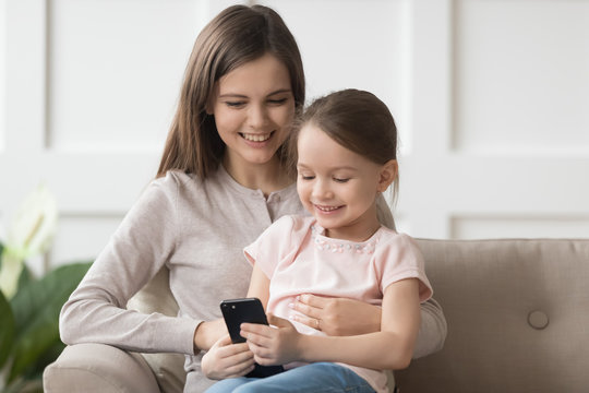 Happy kid daughter and mom enjoy using phone on sofa
