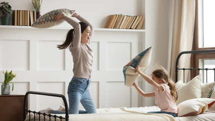 Happy mom and kid daughter having pillow fight on bed