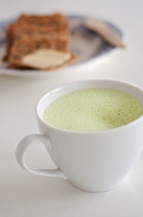 Healthy green tea matcha latte with soy / oat milk decorated with basil and foam on top - a warm beverage to boost brain function and as a cancer prevention! Crisp bread and butter blurry background