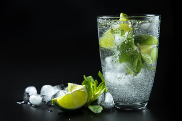 Clear shiny glass filled with ice and delicious Mojito cocktail with lime and mint composed on black background