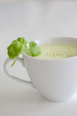 Healthy green tea matcha latte with soy and oat milk in a white tea cup decorated with basil and foam on top - a warm beverage to boost brain function and as a cancer prevention!