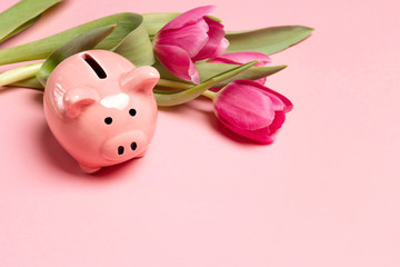 Piggy bank with tulip flowers on pink background.